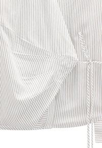 Biały materiał z cienkimi brązowymi pionowymi paskami, z marszczonym wzorem i wiązaniami po jednej stronie do regulacji. Gładka tekstura.