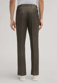 Pantalons marron foncé en tissu texturé, avec une coupe droite, des poches arrière, portés avec des baskets blanches.