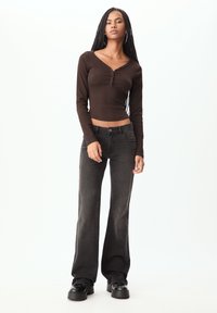 Haut brun à manches longues avec un col en V et des détails en boutons, associé à un jean noir foncé à taille haute et à des chaussures à plate-forme noires.