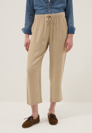 Mujer vistiendo pantalones beige recortados con bolsillos frontales parche, una camisa de mezclilla azul y mocasines marrones con cordones.