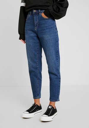 Højtaljede blå denim jeans med lige pasform. Har en knap- og lynlåslukning, subtil falmning og syede detaljer. Sammen med sorte sneakers.