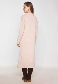 Vestito lungo beige in morbido tessuto a maglia. Presenta un colletto accogliente e polsini a coste. Abbinato a stivali alti fino al ginocchio in suede marrone.