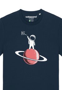 T-shirt en coton bleu marine avec un graphisme d'astronaute faisant signe sur une planète rose avec un anneau blanc, avec le texte "Salut..." au-dessus.
