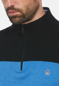 Schwarzer und blauer Halbzip-Pullover mit gerippter Textur, featuring ein Pinguin-Logo auf der linken Brust und einem hohen Kragen.