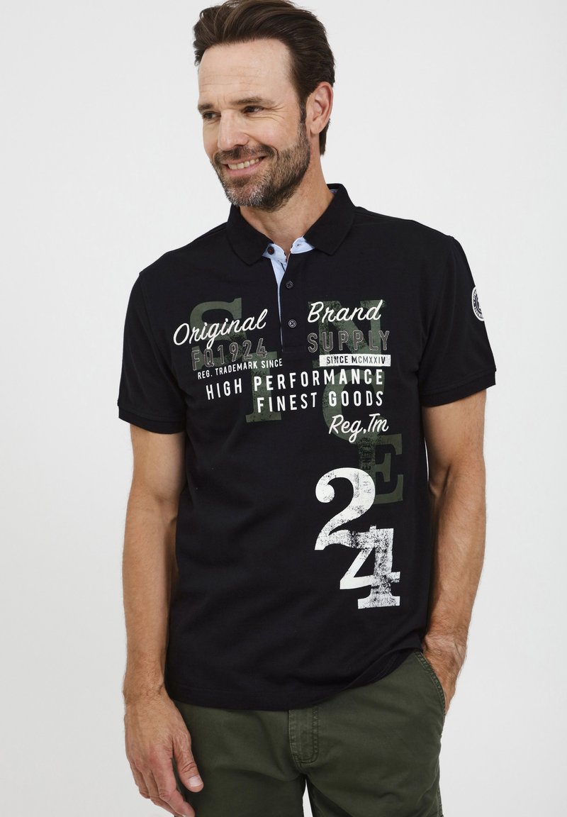 Fekete póló, rövid ujjal, kék színű gallérkiegészítőkkel és különböző színekben és stílusokban megjelenő grafikus szöveggel, beleértve a 24-es és 1924-es számokat.