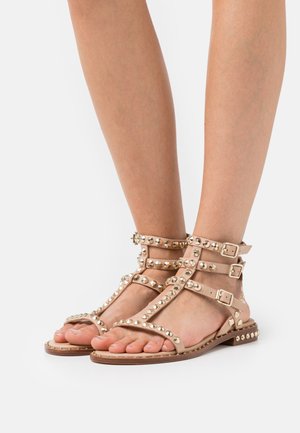 Sandales en cuir tan avec plusieurs brides réglables, des clous métalliques sur les côtés et une semelle plate avec des accents décoratifs.