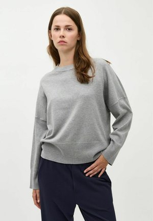 Maglione grigio a maglia con scollatura rotonda, spalle scese e polsini a costine. Abbinato a pantaloni blu scuri per un look casual.