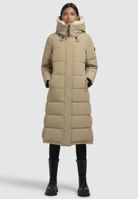 Beige pufains garais mētelis ar augstu apkakli, rāvējslēdzēja aizdari un kabatām. Iezīmēts ar teksturētu, siltu dizainu un noņemamu mākslīgās kažokādas oderi.