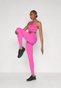 Ehe erkroosad spordirinnahoidja ja retuusid, mis on valmistatud siledast ja venivast kangast. Mustad spordijalatsid tekstuurse mustriga. Modell dünaamilises poosis.