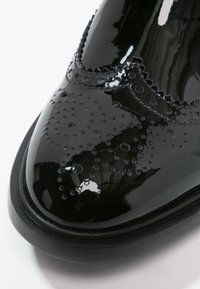 Zapato de vestir de cuero negro brillante con detalles de perforación tipo brogue en la punta redonda y suela negra.