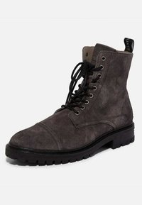 Botte de combat en daim gris à lacets avec un bout arrondi, une semelle en caoutchouc et des œillets en métal. Dotée d'une languette à l'arrière pour un enfilage facile.