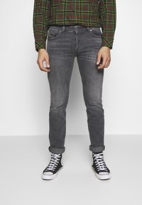 Grå denimjeans med slim fit och lätt slitage. Matchas med uppvikta fållar och svarta högstövlar. En rutig skjorta i grönt och rött bärs.