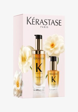 Zestaw olejków do włosów Kérastase Paris Elixir Ultime z butelkami z pompką w kolorze złotym i przezroczystym szkle, przedstawiony na bladoróżowym pudełku z białymi kwiatami.