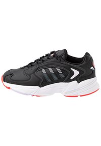 Black athletic sneaker featuring a textured leather upper, white sole, red accents, and striped detailing on the side.