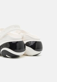 White Crocs with a black glossy heel, featuring a textured upper and adjustable heel strap for a secure fit.
