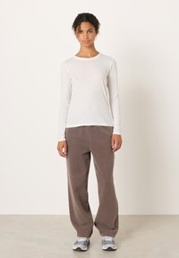 Valge ülipikkade varrukatega ümmarguse kaelusega särk, kombineeritud lahtiste pruuni värvi pükstega. Jalgadel on hallid spordijalatsid mustrilise disainiga.