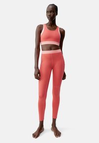 Élénk korall színű sportmelltartó és leggings szett, sima, rugalmas anyaggal, kontrasztos világos őszibarack akcentussal és varrás nélküli kialakítással.