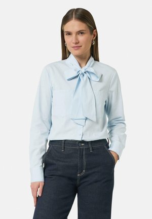 Lichtblauw blouse met een strik-kraag, voorzien van twee voorzakken en lange mouwen. Gepaard met donkerdenim broek.
