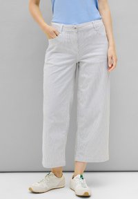 Breite gestreifte Hose aus leichten Stoff mit hoher Taille, seitlichen Taschen und Knopfverschluss, kombiniert mit hellen Sportschuhen.