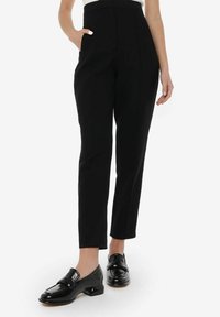 Zwarte op maat gemaakte broeken met een hoge taille, slim fit, zijzakken en een soepele stoftextuur. Gecombineerd met glanzende zwarte instappers.