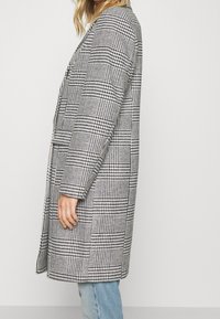 Kariertem Mantel mit schwarz-weißem Schachbrettmuster, langen Ärmeln, offenem Vorderteil und legerem Schnitt. Strukturierter Stoff mit mittellangem Design.
