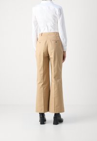 Beige wijde broek gemaakt van katoen, met een hoge taille, achterzakken en gedragen met zwarte blokhak enkellaarsjes.
