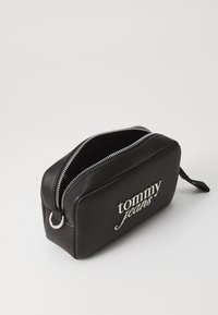 Juodas sintetinis kosmetinis krepšys su sidabriniu užtrauktuku ir "Tommy Jeans" logotipu. Stačiakampio formos, lygia tekstūra, šoninė rankena patogiam nešiojimui.