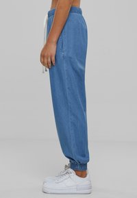 Joggers de mezclilla azul claro con puños y cinturilla elástica, con cordón y bolsillos laterales, combinados con zapatillas deportivas blancas.
