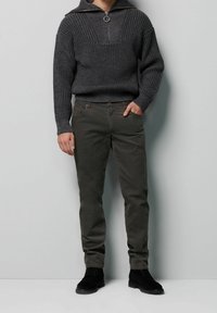 Szary prążkowany sweter z wysokim kołnierzem i zamkiem, zestawiony z oliwkowozielonymi spodniami i czarnymi zamszowymi botkami. Prosta, dopasowana sylwetka.