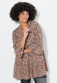 Tunic con motivo floreale su sfondo scuro; i colori vivaci includono rosa, arancione e bianco. Presenta maniche lunghe e un design a strati.