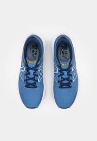 Baskets de sport bleues avec une tige en maille texturée, semelles blanches, lacets contrastés et logo sur la languette et les semelles intérieures.
