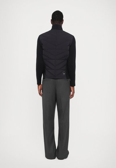 Dark puffer jacket with a high collar, featuring a quilted design on the back, paired with gray tailored trousers with a straight cut.