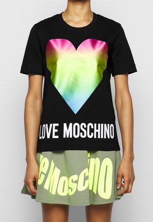 Osoba nosící černé tričko s velkým duhovým srdcem a nápisem "LOVE MOSCHINO", doplněné zelenou sukní s velkým žlutým nápisem.