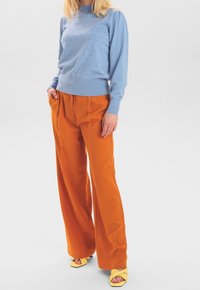 Ljusblå stickad tröja med puffärmar och små mönstrade hål, i kombination med högmidjade oranga vida byxor och gula sandaler.