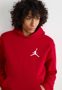 Rød hættebluse lavet af bomuld med en forlommer, prydet med et hvidt Jumpman-logo på venstre bryst. Blød tekstur og afslappet pasform.