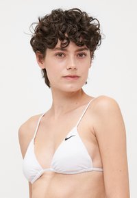Biely trojuholníkový bikiny horný diel s tenkými nastaviteľnými ramienkami. Obsahuje zhromaždené stred a malé čierne logo Nike na ľavej strane.