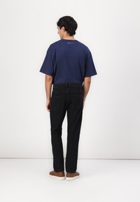 Tricou de culoare albastru închis, cu mânecă scurtă, croială lejeră, combinat cu blugi negri și pantofi slip-on maro. Cusături vizibile și detaliu logo pe spate.
