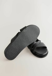 Schwarze Slide-Sandalen mit strukturiertem schwarzem Gummisohlenprofil, ausgestattet mit zwei breiten Riemen über dem Spann. Glattes Lederobermaterial mit feiner Naht.