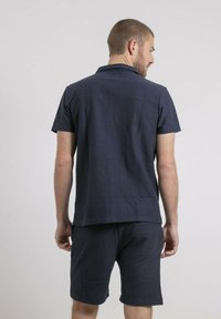 Chemise à manches courtes marine en tissu texturé, assortie à un short. Présente une coupe droite avec un col.