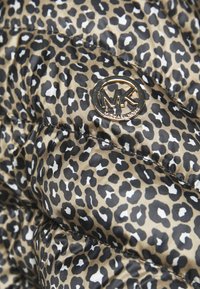 Vêtements d'extérieur matelassés avec un motif léopard en beige, noir et blanc. Présente un logo circulaire doré avec "MK" sur le tissu.