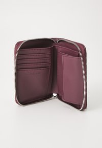 Bordo kožni novčanik s zatvaračem na zip, s više mjesta za kartice i džepom za identifikaciju, s diskretnim utisnutim logotipom unutra. Glatka tekstura.