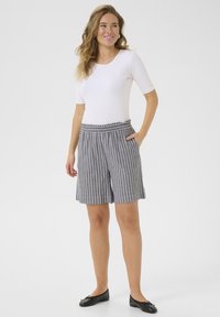 Shorts rayés gris et blanc avec une taille élastique et des poches latérales, associés à un haut blanc ajusté et des chaussures plates noires.