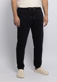 Zwarte trainingsbroek met een elastische tailleband en een trekkoord. Geaccentueerd met zilveren hardware, gecombineerd met crèmekleurige instap schoenen.
