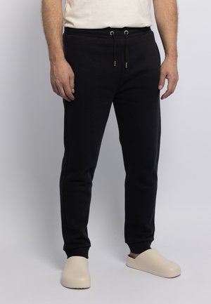 Black sweatpants with an elastic waistband and drawstring. Accented with silver hardware, paired with cream-colored slip-on shoes.