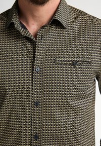 Overhemd met knopen en een geometrisch zwart-goud patroon, met kraag en borstzak. Beschikt over zwarte knopen en een gladde textuur.