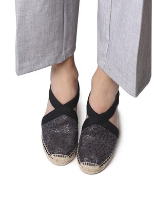 Musthave musta espadrillide kingad lillemustriga ja punutud jute tallaga. Elastsed risti-rihmad üle jala tekstureeritud pinnaga.