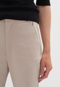 Bežové kalhoty vyrobené z hladkého materiálu, se bočními kapsami a slim-fit střihem, spárované s černým strukturovaným pleteným topem.