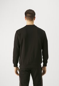 Felpa nera con scollo rotondo, maniche lunghe e polsini a costine. Texture liscia, caratterizzata da una vestibilità leggermente rilassata, indossata con pantaloni coordinate.