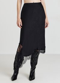Jupe midi noire avec un ourlet asymétrique, ornée de dentelle au bas et d'une surface texturée. Portée avec des bottes noires montantes.