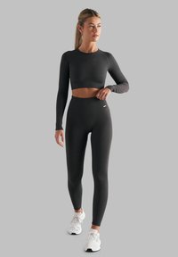 Svart ribbet langermet crop topp sammen med høyhentede leggings, begge laget av elastisk stoff. Hvite sportssko fullfører antrekket.